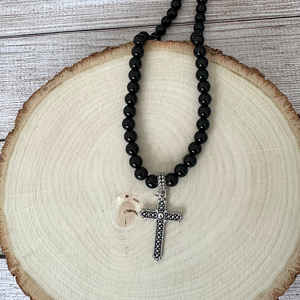 Black Onyx Silver Textured Cross Mens Beaded Necklace, displayed on a round natural wood slice against a weathered wood plank background.