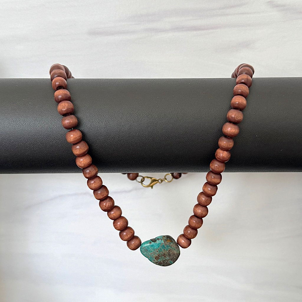 Brown Wood and Turquoise Stone Beaded Mens Necklace draped over a black cylindrical display stand on a light gray marble surface.