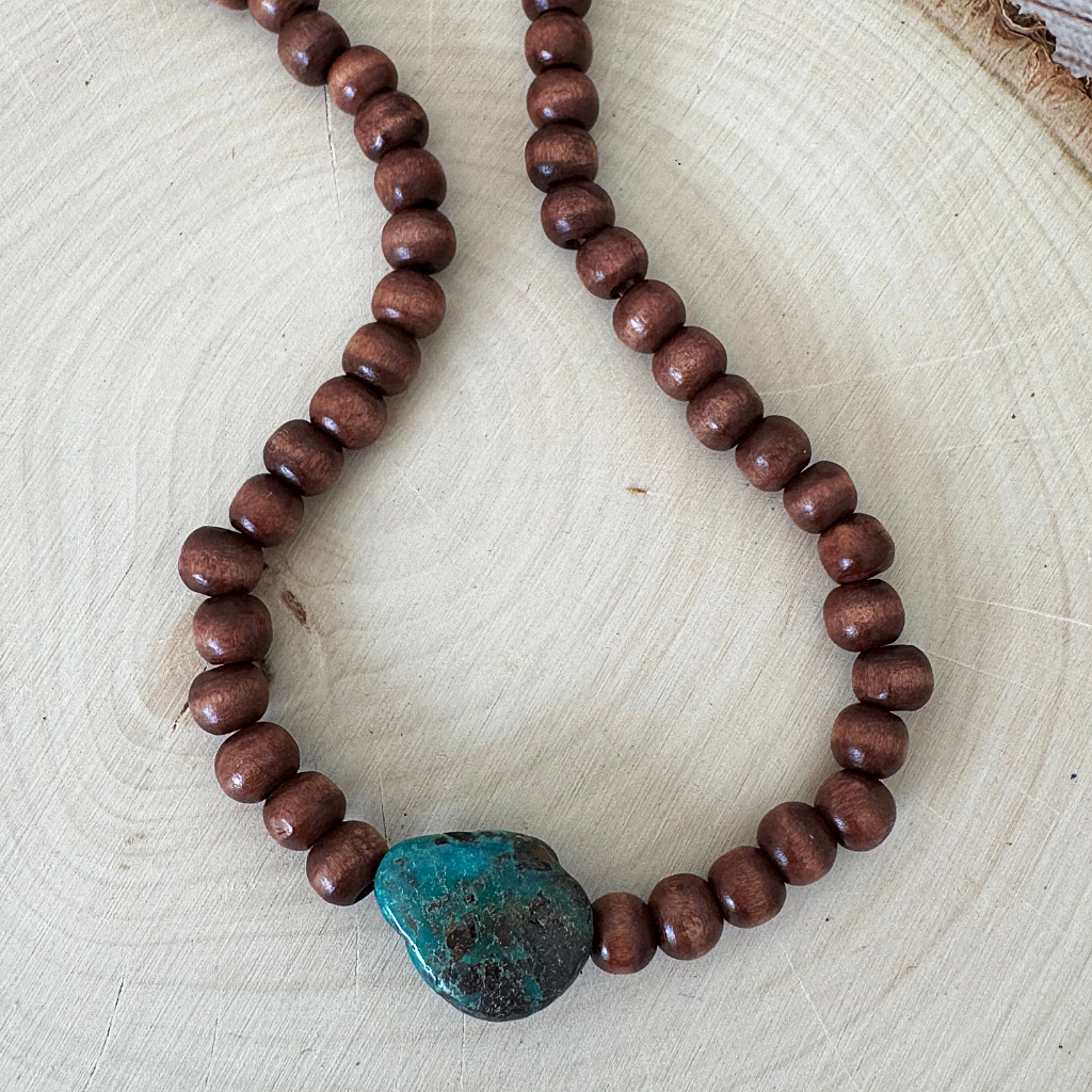 Brown Wood and Turquoise Stone Beaded Men's Necklace displayed on a light wood slice background.