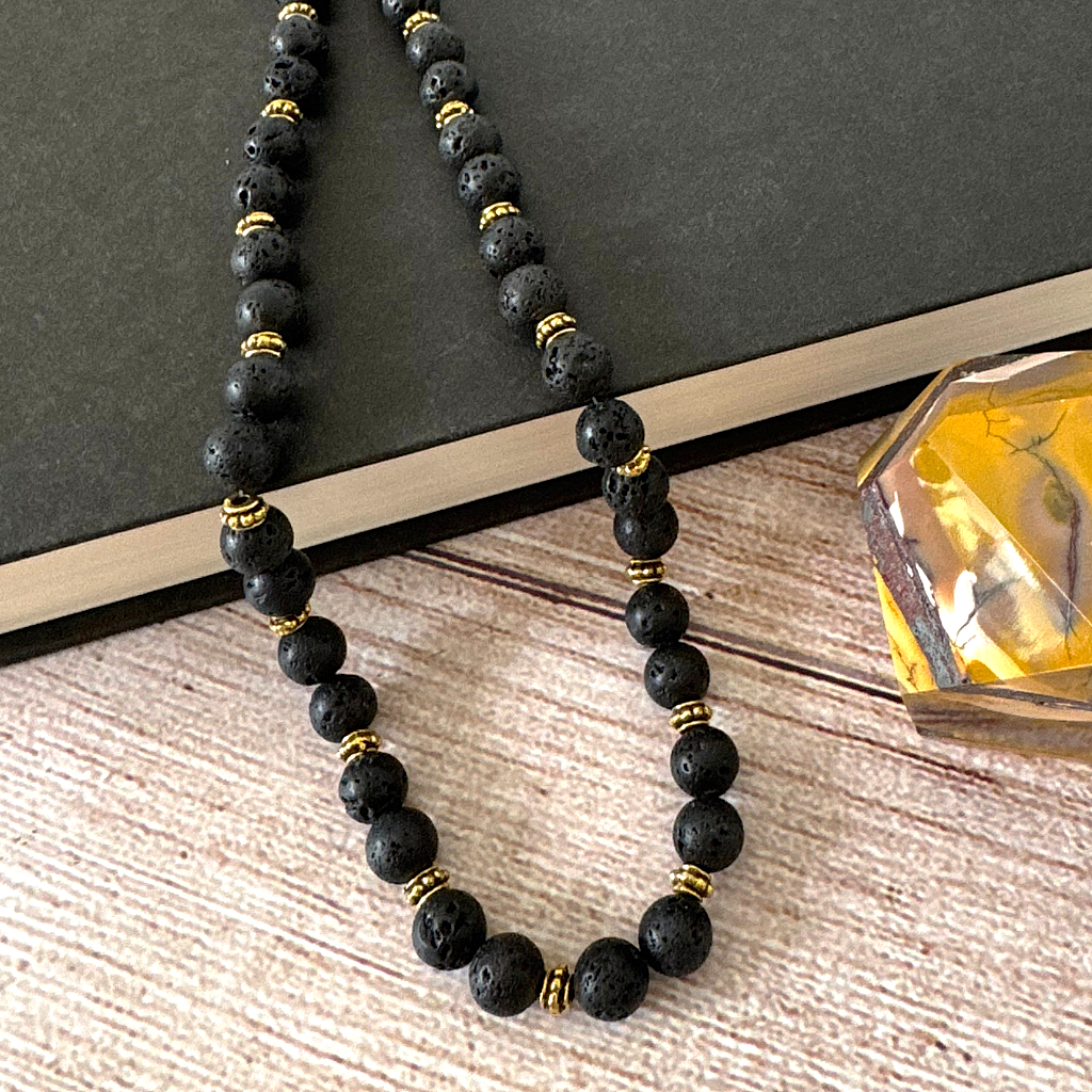 Mens Black Lava and Gold Beaded Necklace on a wooden surface