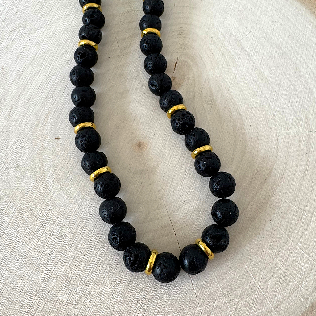Mens Black Lava and Gold Ring Beaded Necklace on a light wooden surface