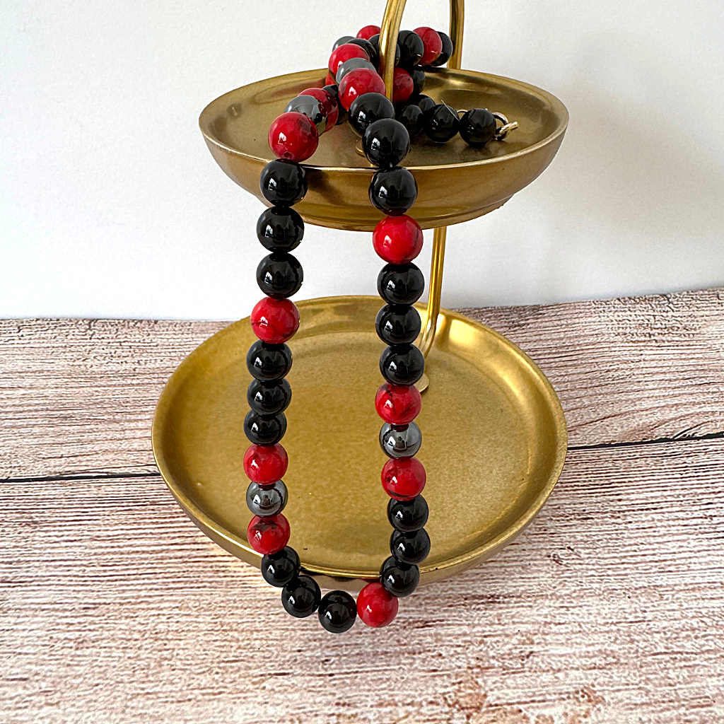 Mens Black Onyx and Red Mosaic Beaded Necklace on a gold stand against a white background