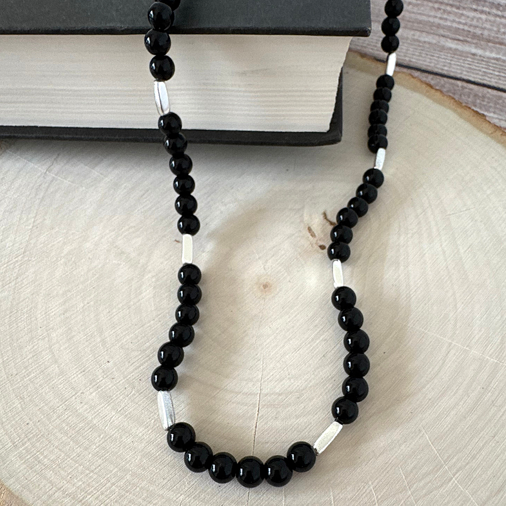 Mens Black Onyx and Silver Tube Beaded Necklace on a wooden surface with a book in the background