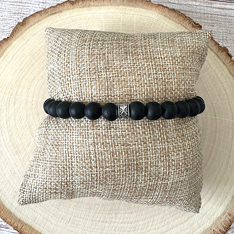 Mens Matte Black Onyx Beaded Bracelet with Silver Bead On a Beige Pillow