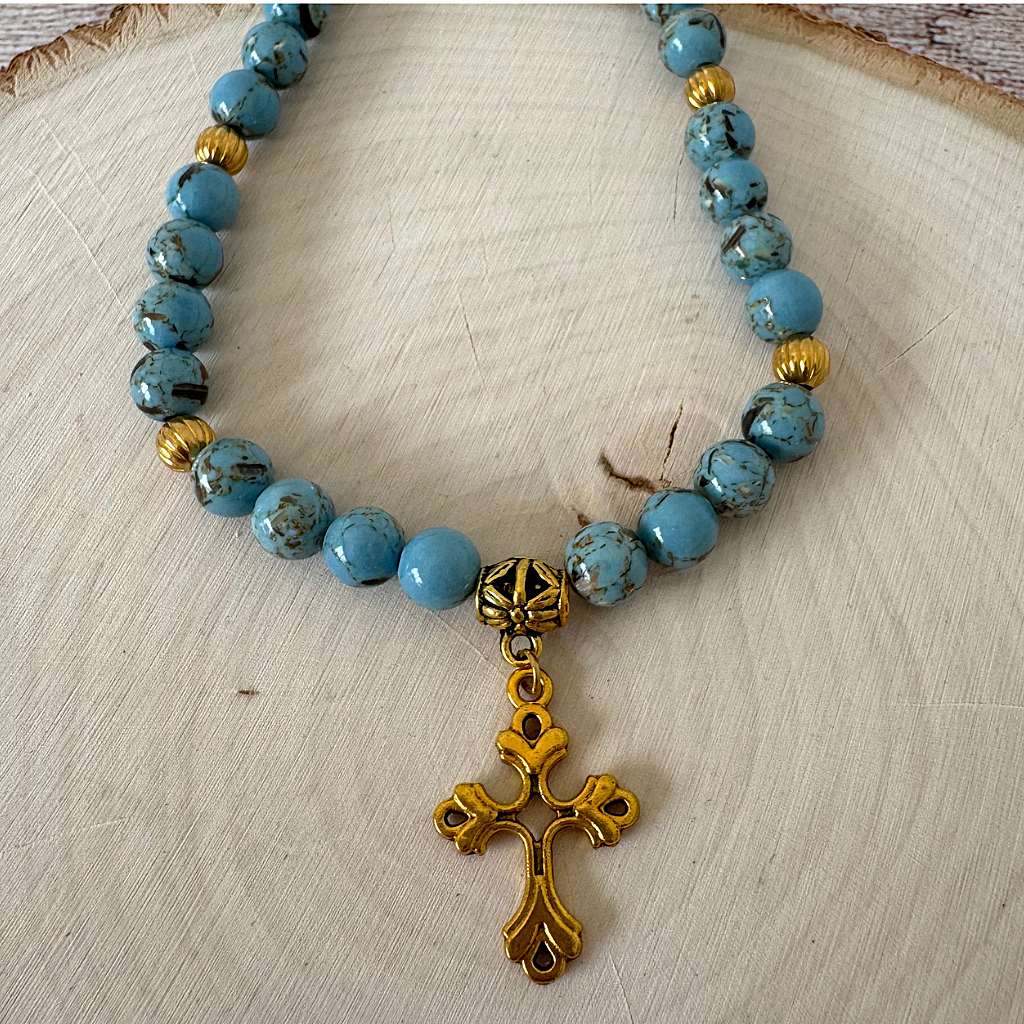 Mens Sky Blue Howlite and Shell Necklace With Gold Cross on a wooden surface