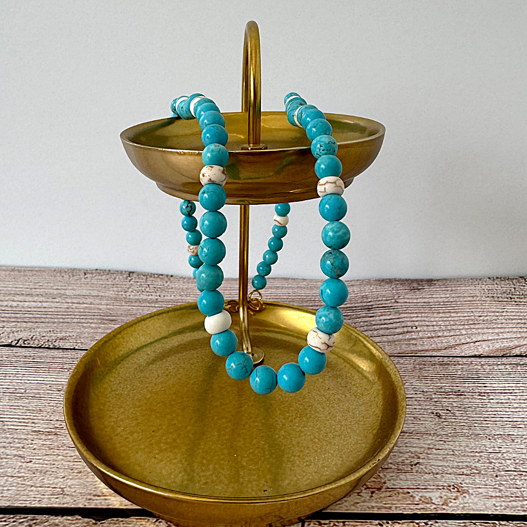 Turquoise Blue and White Magnesite Beaded Necklace on a gold jewelry stand against a white background