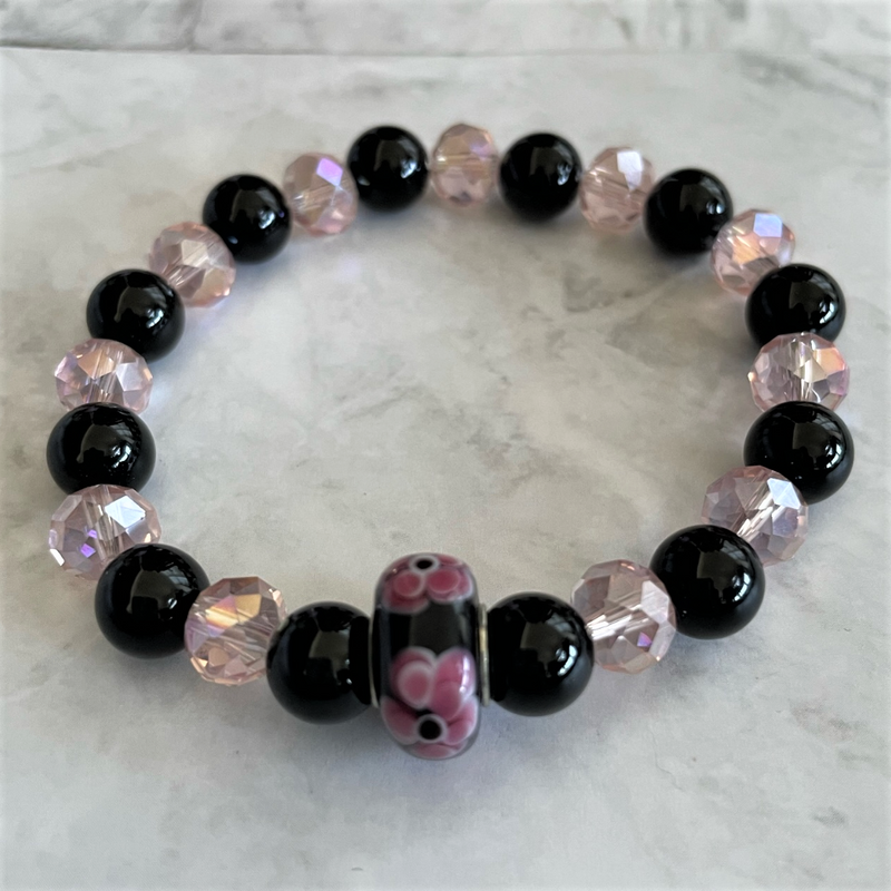 A bracelet with a combination of black onyx and pink crystal beads, featuring a large black flower-shaped bead in the center.