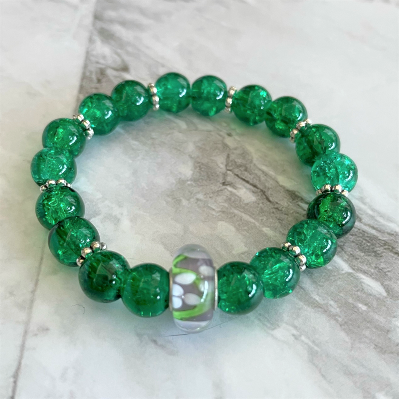 A green glass beaded bracelet with silver flower rondelles and a large flower design bead in the center.