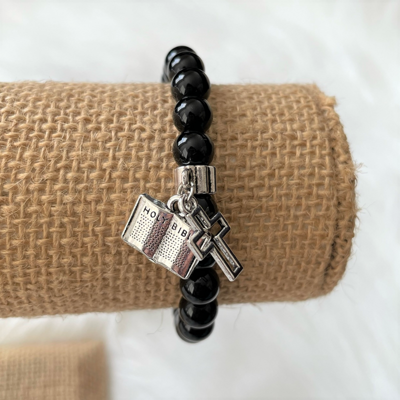 A men's bracelet featuring black onyx beads, a silver cross, and a Bible charm.