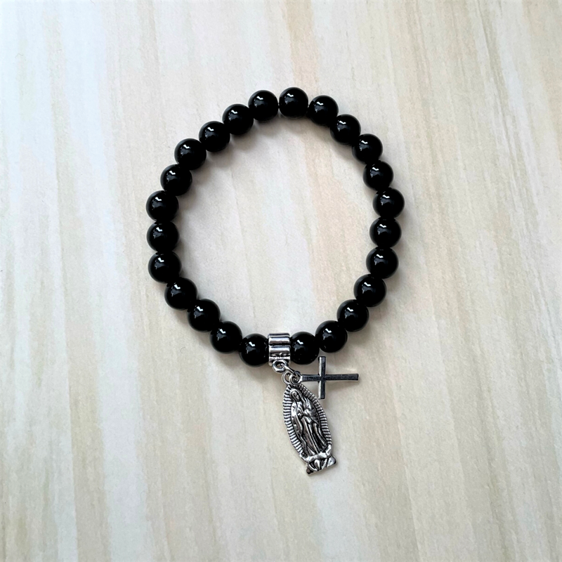 A men's bracelet with black onyx beads and two silver charms, one of which is a cross and the other is a Saint Mary medal.
