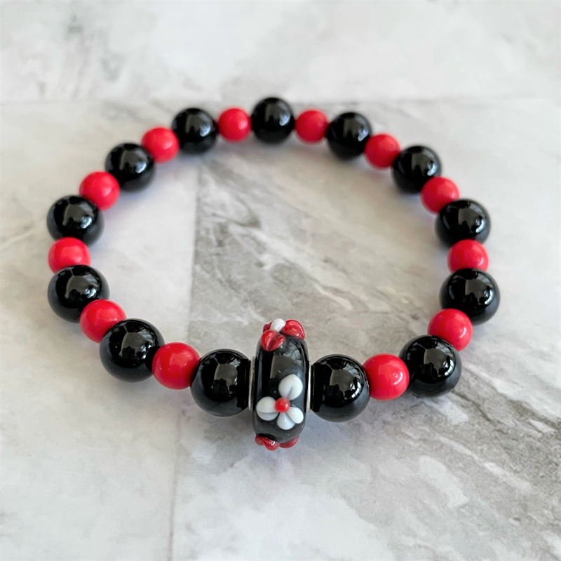 A red and black womens beaded stretch bracelet with a glass center bead designed with 3D flowers.