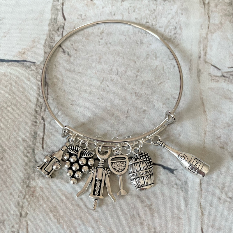 Adjustable silver bangle bracelet with a series of wine-themed charms including grapes, a wine glass, a wine bottle, and corkscrews.